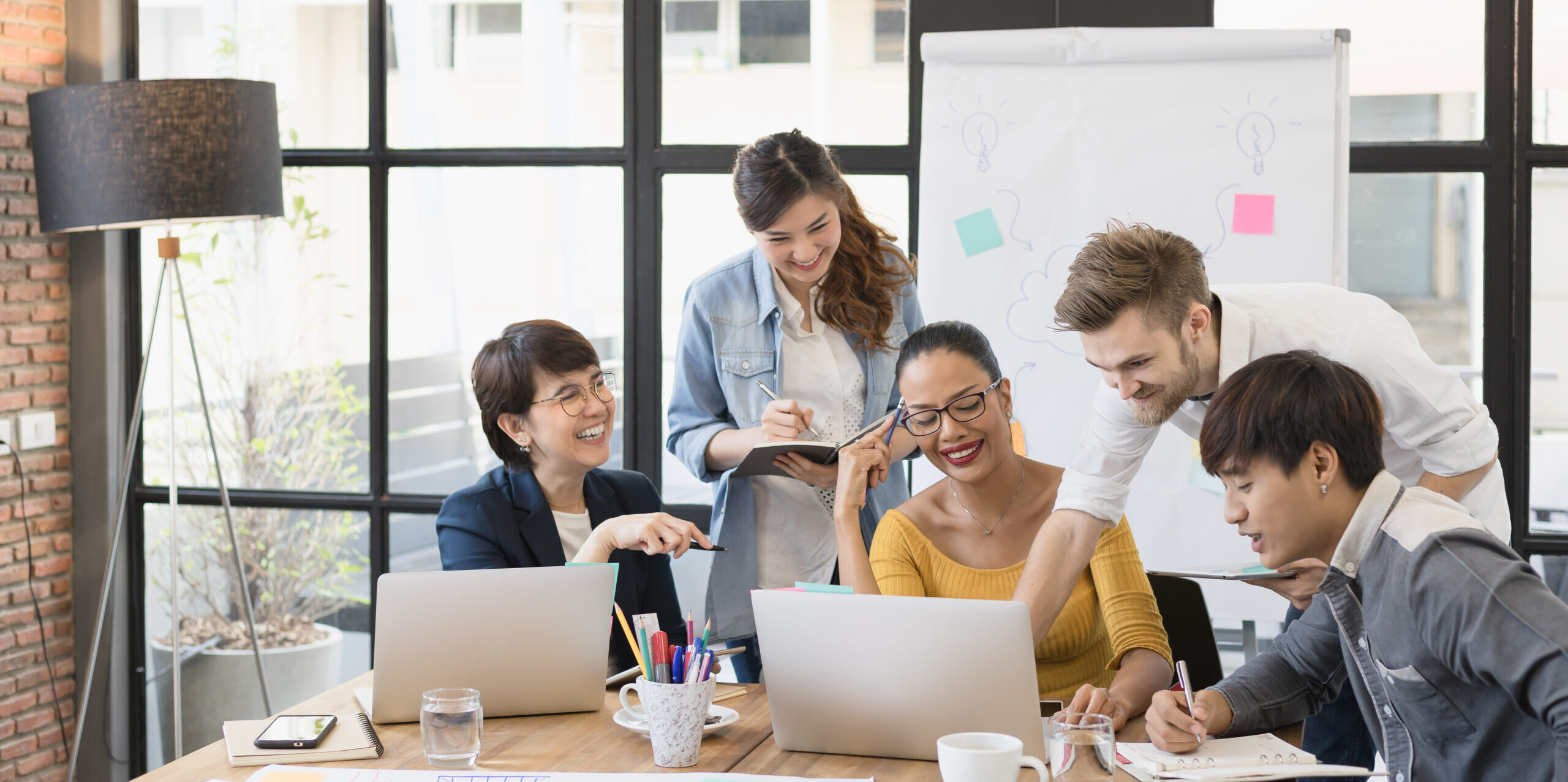 group of happy business people working together, meeting and brainstorming in office. Use computer, laptop, tablet, mobile phone.